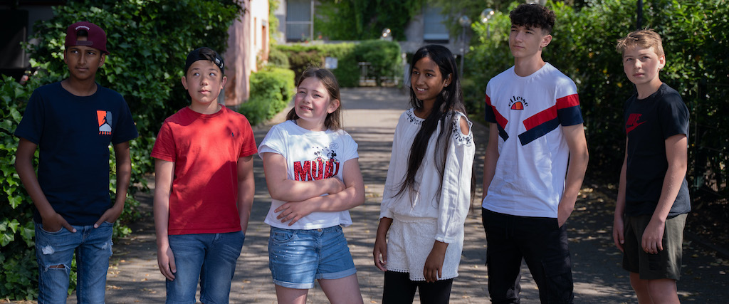 sechs glückliche Kinder, im Alter von 10 bis 12 Jahren, stehen nebeneinander, lachen und blicken in die Ferne